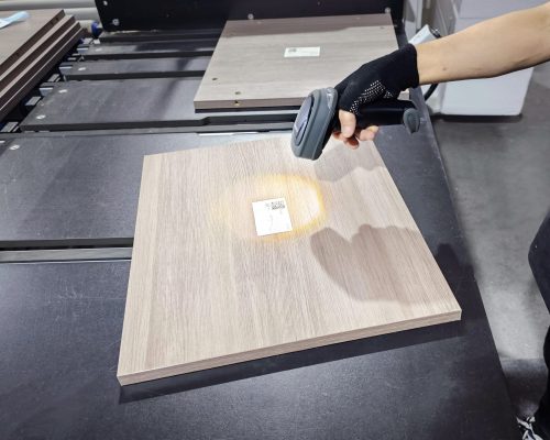 A worker using a scanner to scan a QR code sticker on a panel along the production line at Jilphar Home’s kitchen cabinet factory, demonstrating the integration of automation and quality control in the manufacturing process.
